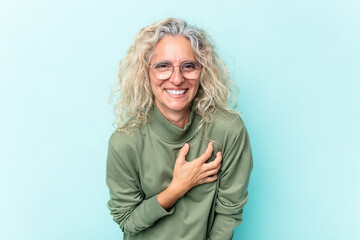 Middle age caucasian woman isolated on blue background laughs out loudly keeping hand on chest.