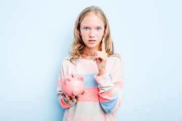 Caucasian teen girl holding a piggybank isolated on blue background having an idea, inspiration concept.