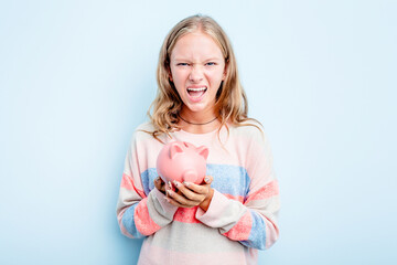 Obraz na płótnie Canvas Caucasian teen girl holding a piggybank isolated on blue background screaming very angry and aggressive.