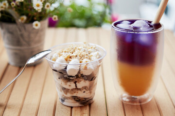 Trendy purple and yellow cocktail with dessert and straw reed. Anchan blue tea - antioxidants and detox water with light dessert in a disposable cup at the terrace on the wooden table