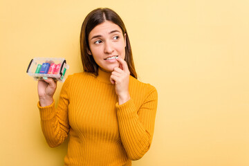 Young caucasian woman holding a batteries box isolated on yellow background relaxed thinking about something looking at a copy space.