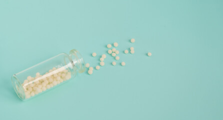 Alternative homeopathy medicine concept. Homeopathic globules scattered from a clear glass bottle on light blue background, copyspace for text. Healtcare and pills concept