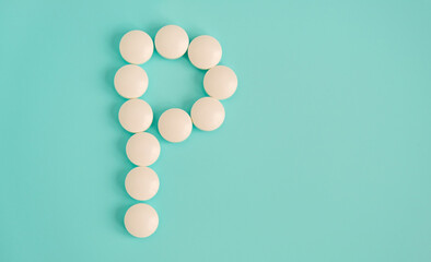 Letter P made from white pills on a blue background. White medical pills. Macro top view with copy space. Health care and pills concept, pharmaceutical, disease prevention