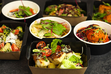 Ready healthy food menu in lunch boxes with fish, meat and vegetable packages as daily courier delivery diet plan isolated on black table background. The concept of ordering takeaway containers.