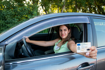 Teenager girl  showing his driver's license in the car window after passing the exam or at the request of the traffic police