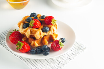 Fresh homemade food of berry Belgian waffles with honey, chocolate, strawberry, blueberry, maple syrup and cream. Healthy dessert breakfast concept with coffee