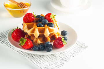 Fresh homemade food of berry Belgian waffles with honey, chocolate, strawberry, blueberry, maple syrup and cream. Healthy dessert breakfast concept with coffee