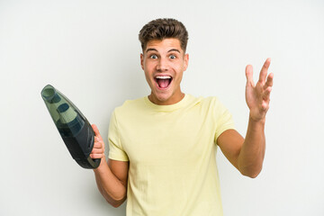 Young caucasian man holding a hand vacuum cleaner isolated on white background receiving a pleasant...