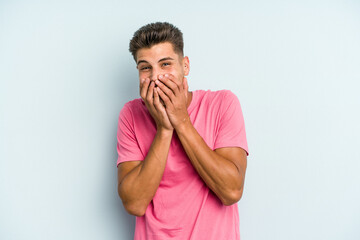 Young caucasian man isolated on blue background laughing about something, covering mouth with hands.