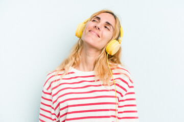 Young caucasian woman listening to music isolated on blue background dreaming of achieving goals...