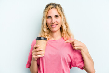 Young caucasian woman holding a take away coffee isolated on blue background person pointing by hand to a shirt copy space, proud and confident