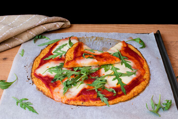 Pizza con base de coliflor con salsa de tomate, queso mozzarella fresca, y rúcula. Una porción cortada y puesta encima.