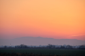 Beautiful evening panoramic landscape with bright setting sun over distant mountain peaks at sunset