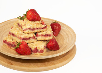 Strawberry crumb bars homemade and fresh strawberries are on a wooden platter against a white background.