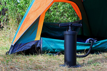 air mattress pump with a tent on a background in a pine forest in the summer, a man pumps up a mattress, a pump between his legs, the pump inflates the mattress, the pump inflates the air mattress in 