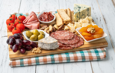 Appetizer board with cheese, nuts, fruits, toasts and charcuterie over wooden table