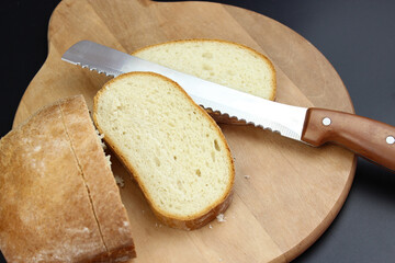 A large knife cuts thin pieces of white bread from a rectangular loaf.