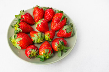 Red ripe strawberries in a light green bowl, light background, top view, healthy food, natural...