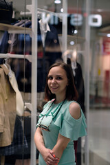 Woman choosing clothes in shop. Side view of young female customer in casual clothes standing near wardrobe with clothes.