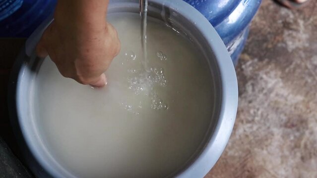 The cook uses her finger to measure the water level as she pours water into the rice cooker.