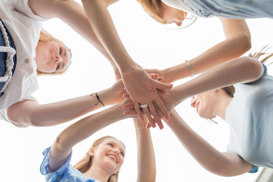 Bottom view of young wonderful women folding stacking joining hands on sky background. Symbol of unity, friendship.