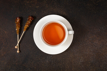A cup of black tea and caramel sugar on brown background. Top view. Copy space.