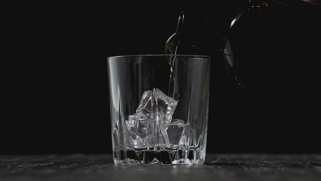 Golden whiskey pouring in glass in slow motion. Pouring whisky from bottle on black background. Alcohol concept