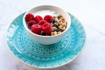 Granola with raspberries and greek yogurt in a bowl on white marble table background. Top view, flat lay, copy space. Healthy breakfast concept.