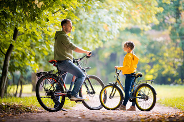 Naklejka premium Happy father and daughter walk with bicycles in the autumn park on a sunny day.