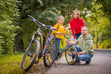 Dad, mom and daughter walk with their bicycles along autumn path of the park.