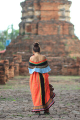 An elderly woman in traditional woven clothes is walking to see the scenery of an ancient city in Thailand and wants to dress in traditional woven clothes to match the atmosphere of the ancient city.