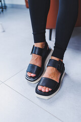 Women's legs close-up in black leather sandals made of genuine leather.Collection of women's summer shoes