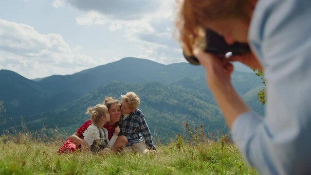 Man photographing woman kids in front mountains. Family enjoying photo session.