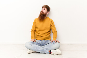 Young caucasian man sitting on the floor isolated on white background dreaming of achieving goals...