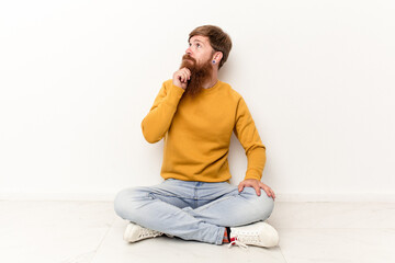 Young caucasian man sitting on the floor isolated on white background looking sideways with doubtful and skeptical expression.