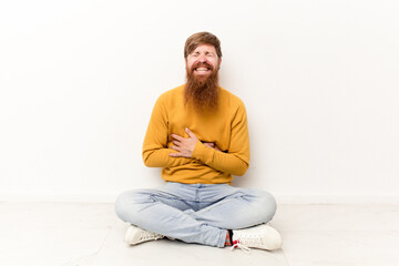 Young caucasian man sitting on the floor isolated on white background laughing and having fun.