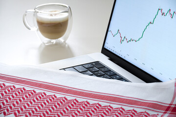 Focus on laptop screen with charts, coffee, and Saudi scarf, headdress