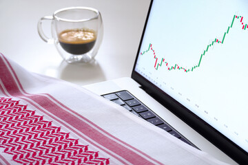 Focus on laptop screen with charts, coffee, and Saudi scarf, headdress