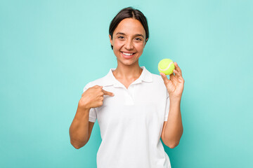 Young hispanic physiotherapy holding a tennis ball isolated on blue background person pointing by hand to a shirt copy space, proud and confident