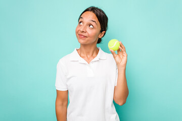 Young hispanic physiotherapy holding a tennis ball isolated on blue background dreaming of...