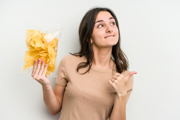 Young caucasian woman holding crisps isolated on yellow background points with thumb finger away, laughing and carefree.