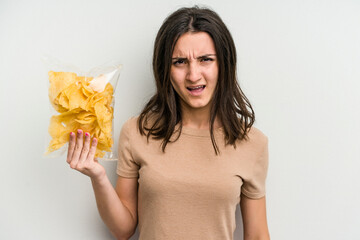 Young caucasian woman holding crisps isolated on yellow background screaming very angry and aggressive.