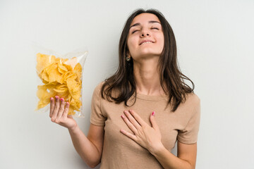 Young caucasian woman holding crisps isolated on yellow background laughs out loudly keeping hand...