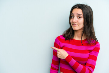 Young caucasian woman isolated on blue background smiling and pointing aside, showing something at blank space.
