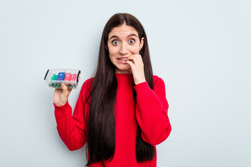 Young caucasian woman holding a batteries box isolated on blue background biting fingernails, nervous and very anxious.