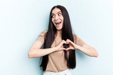 Young caucasian woman isolated on blue background smiling and showing a heart shape with hands.