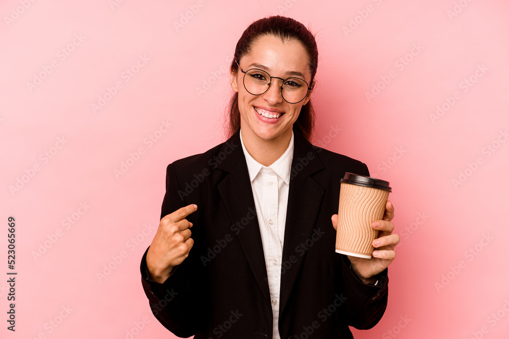 Wall mural Young business caucasian woman holding take away coffee isolated on pink background person pointing by hand to a shirt copy space, proud and confident