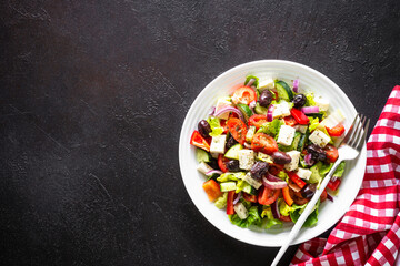 Greek salad. Vegetable salad with tomato, cucumber, feta cheese and olive oil. Top view on black stone table.