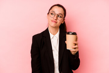 Young business caucasian woman holding take away coffee isolated on pink background dreaming of...