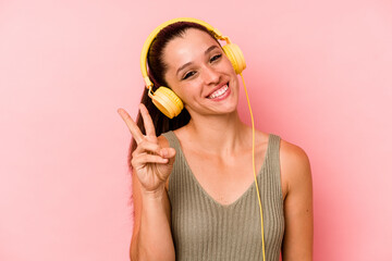 Young caucasian woman listening to music isolated on pink background joyful and carefree showing a peace symbol with fingers.